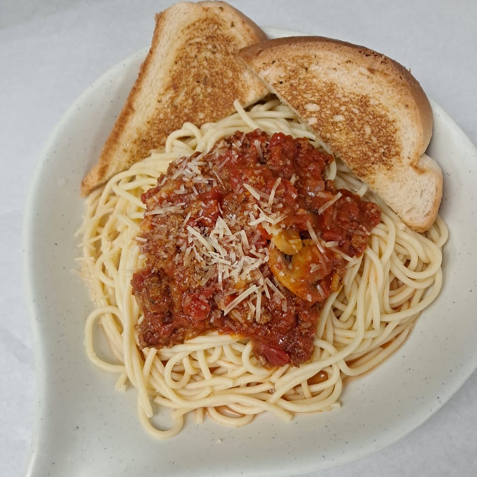 Spaghetti with meat sauce and grated cheese, served with two slices of toasted bread.