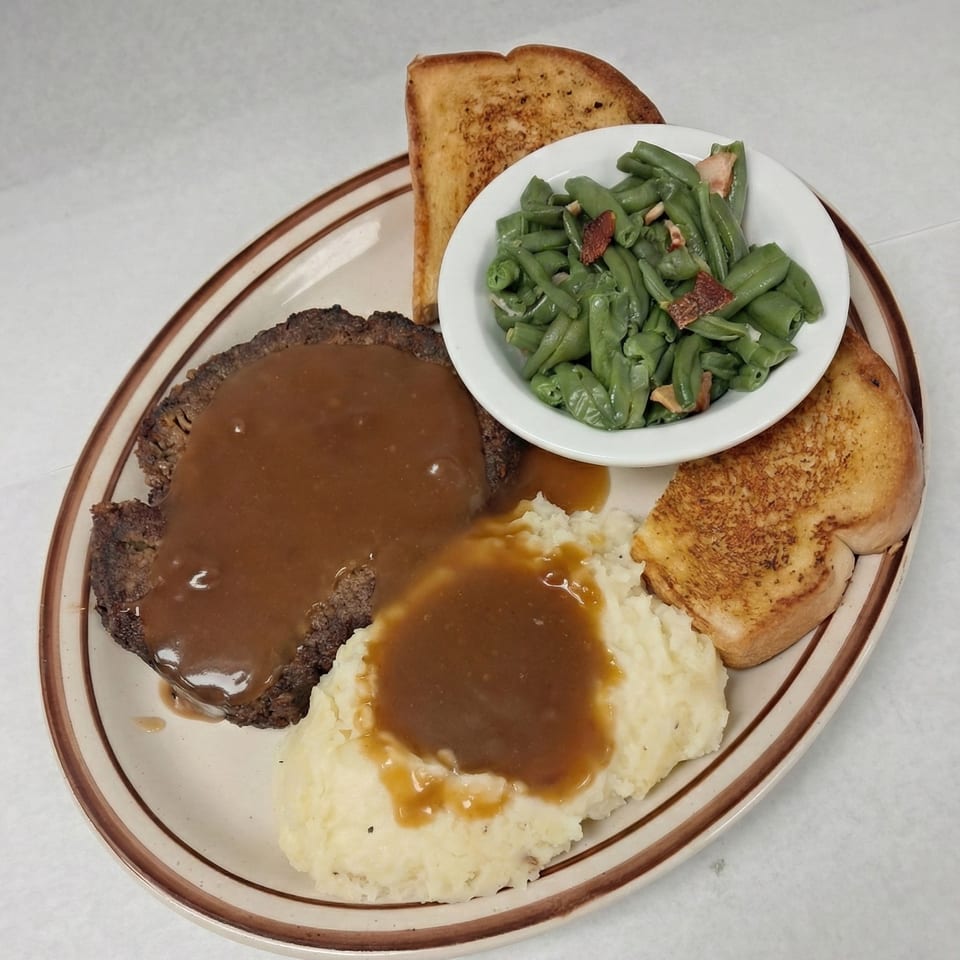 Salisbury steak with gravy, mashed potatoes, green beans, and Texas toast on a plate.